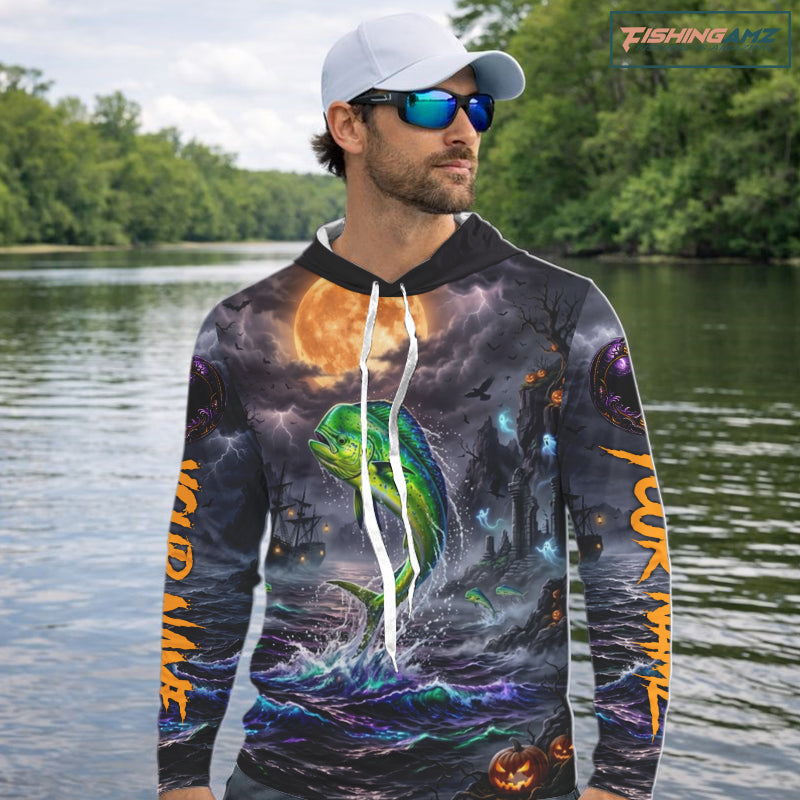 A long-sleeve hoodie with an all-over Halloween-themed graphic print featuring a green mahi-mahi fish jumping from dark ocean waves under a large orange full moon, with spooky ships and lightning in the background. The hoodie has white drawstrings and a white inner hood lining, shown on a plain white background with a FishingAmz logo in the top right corner.