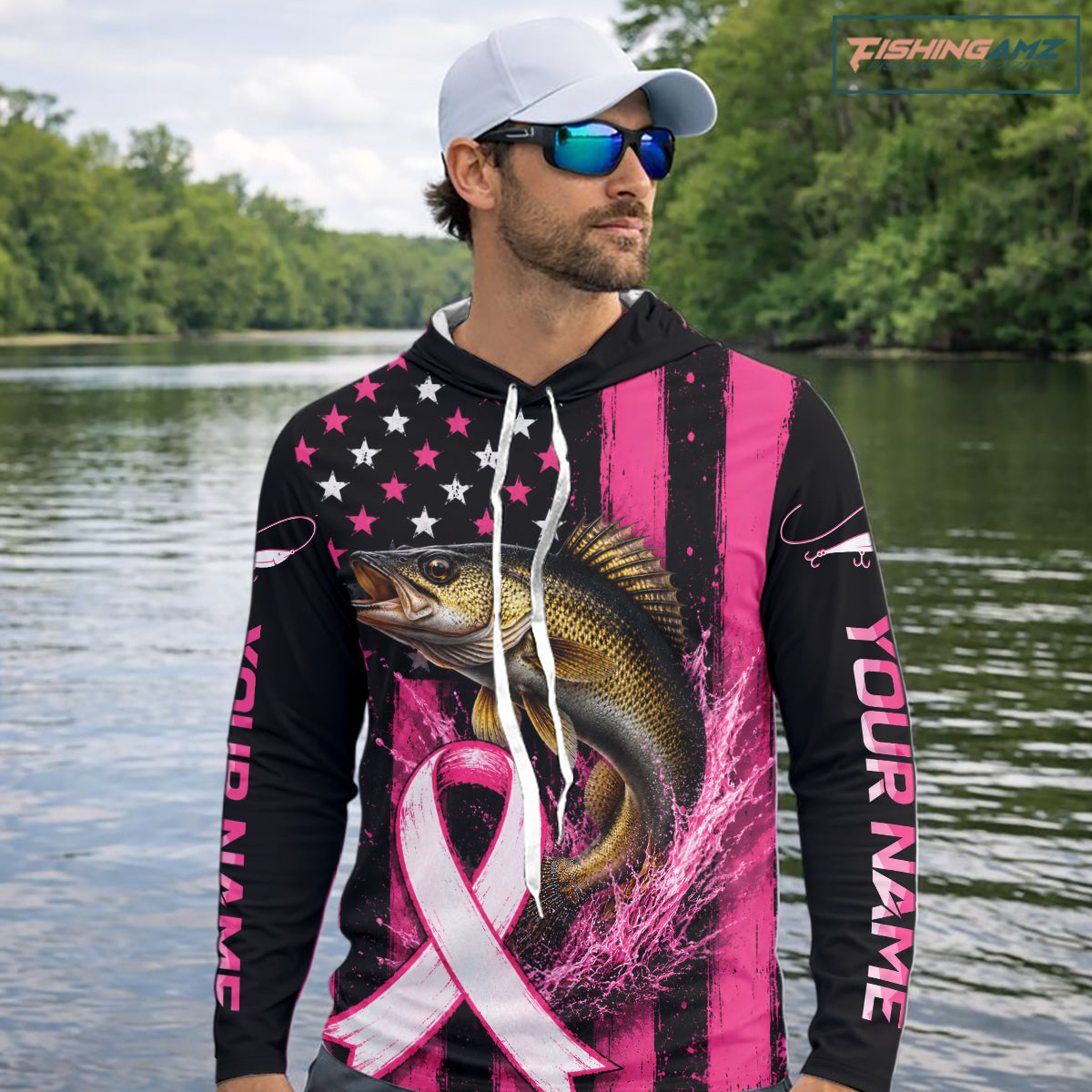 A man wearing a black and pink long-sleeve hoodie with a walleye fish graphic and pink ribbon design on the back, standing on a boat with fishing rods and the ocean in the background.