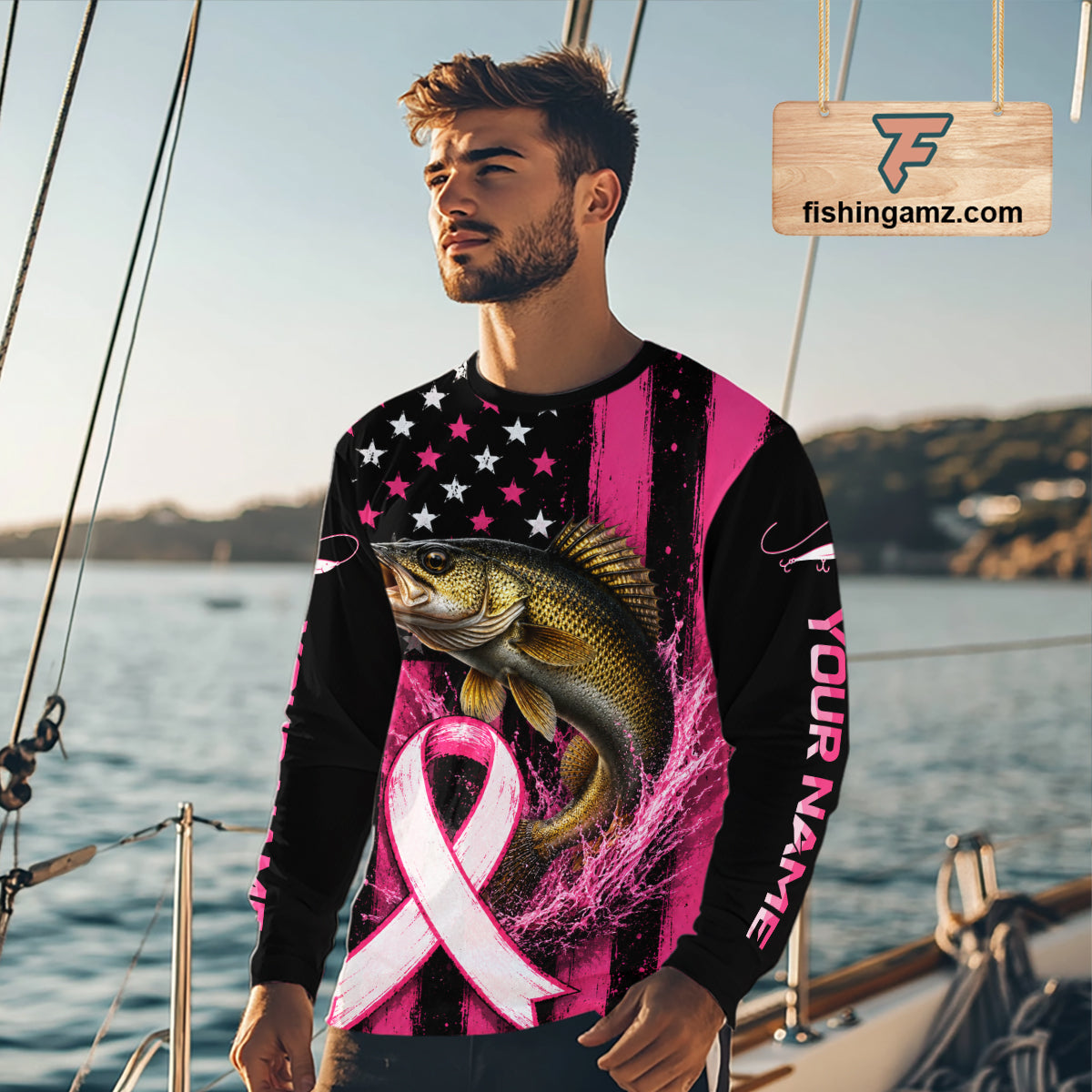 A man wearing a long-sleeve black and pink graphic shirt with a large fish and pink ribbon print, standing on a boat deck with water and boats in the background.