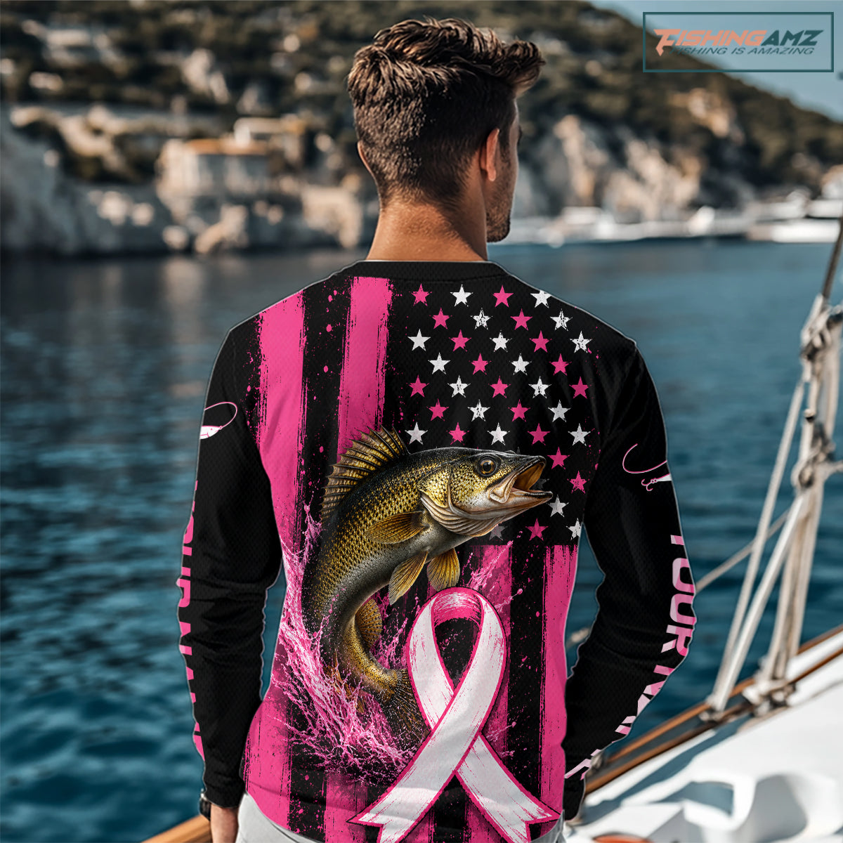 A man wearing a long-sleeve black and pink graphic shirt with a large fish and pink ribbon print, standing on a boat deck with water and boats in the background.