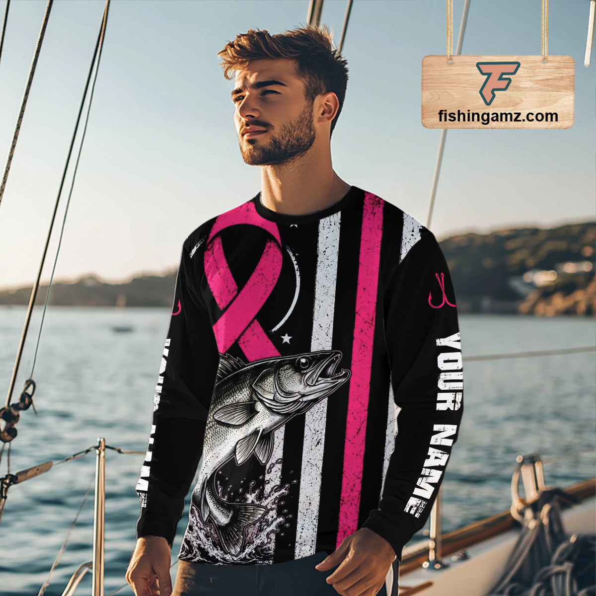A man wearing a long-sleeve custom graphic shirt on a boat deck, featuring a black and white striped design with a pink ribbon, a fish graphic, and 'YOUR NAME' printed vertically.