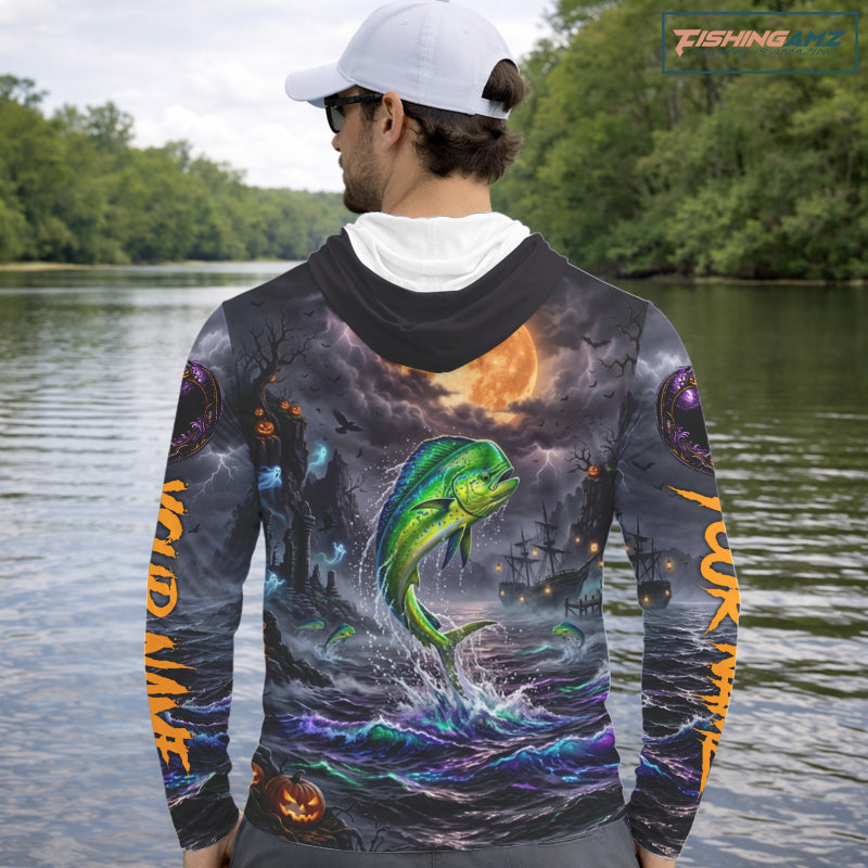 A man on a boat wearing a long-sleeve hoodie with a detailed all-over graphic print. The design features a green mahi-mahi fish jumping from purple and blue ocean waves under a full moon, with fishing ships and lightning in the background.
