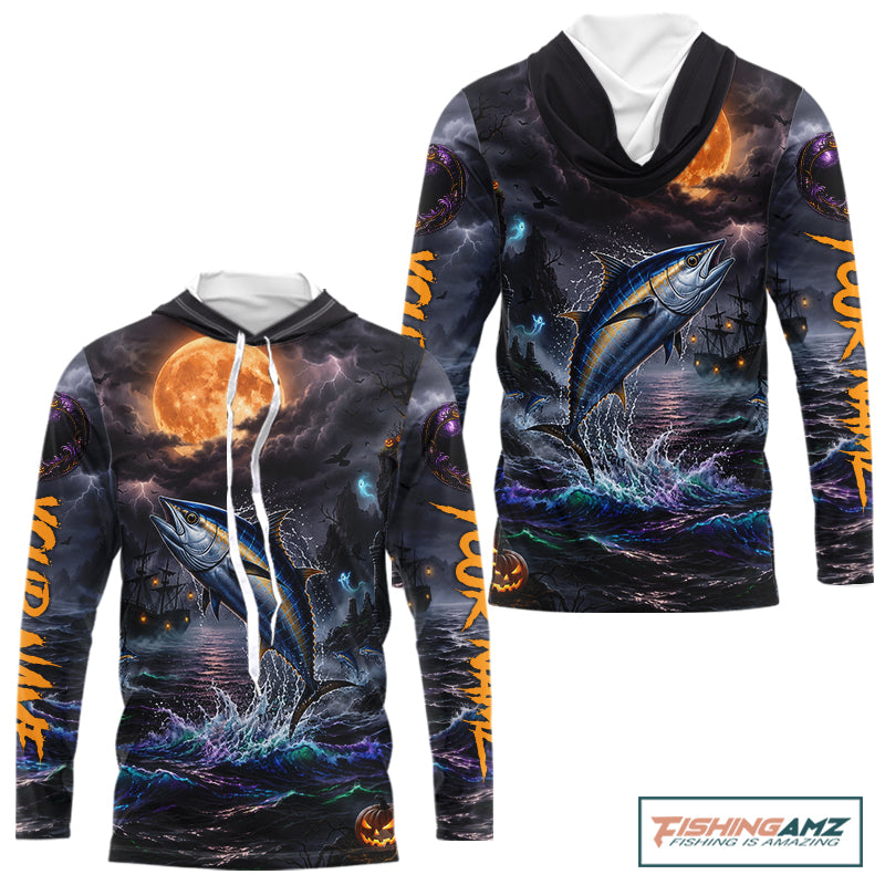 A long-sleeve hoodie with an all-over Halloween-themed graphic print featuring a tuna jumping fish under a full moon, dark stormy sky, lightning, and orange text on the sleeves. The hoodie has a white drawstring and is shown on a plain white background with a FishingAmz logo in the top right corner.