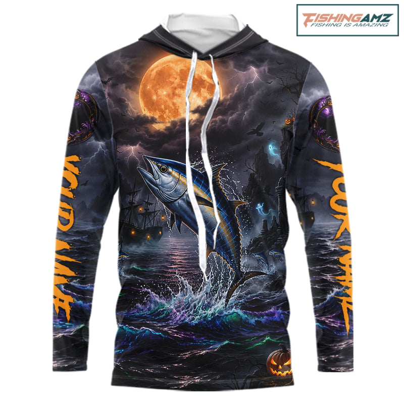 A long-sleeve hoodie with an all-over Halloween-themed graphic print featuring a tuna jumping fish under a full moon, dark stormy sky, lightning, and orange text on the sleeves. The hoodie has a white drawstring and is shown on a plain white background with a FishingAmz logo in the top right corner.