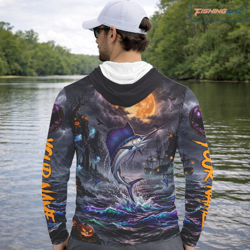 A man wearing a dark navy blue hoodie with a highly detailed, colorful graphic print on the back and sleeves. The print features a marlin jumping from the ocean, a large orange full moon, storm clouds, and pirate ships.