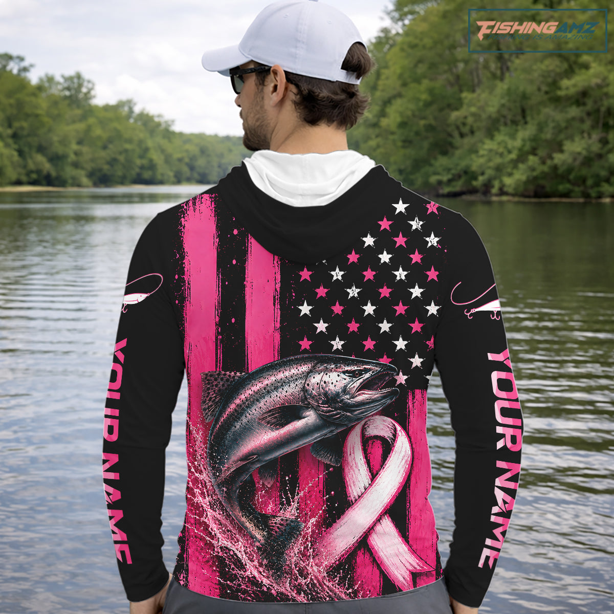 A man on a boat wearing a black long-sleeve hoodie with a pink and white patriotic fish graphic on the back, featuring stars, stripes, and a pink ribbon. He is wearing a dark blue cap and sunglasses, with fishing rods visible in the background.