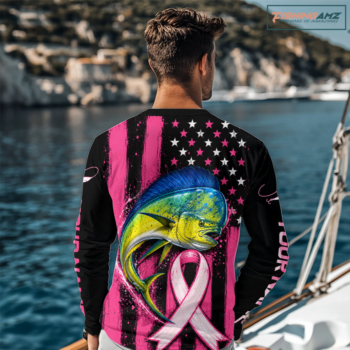 A man viewed from behind wearing a long-sleeve black and pink graphic shirt with a large mahi mahi, pink ribbon, stars, and vertical 'YOUR NAME' text, standing by the ocean