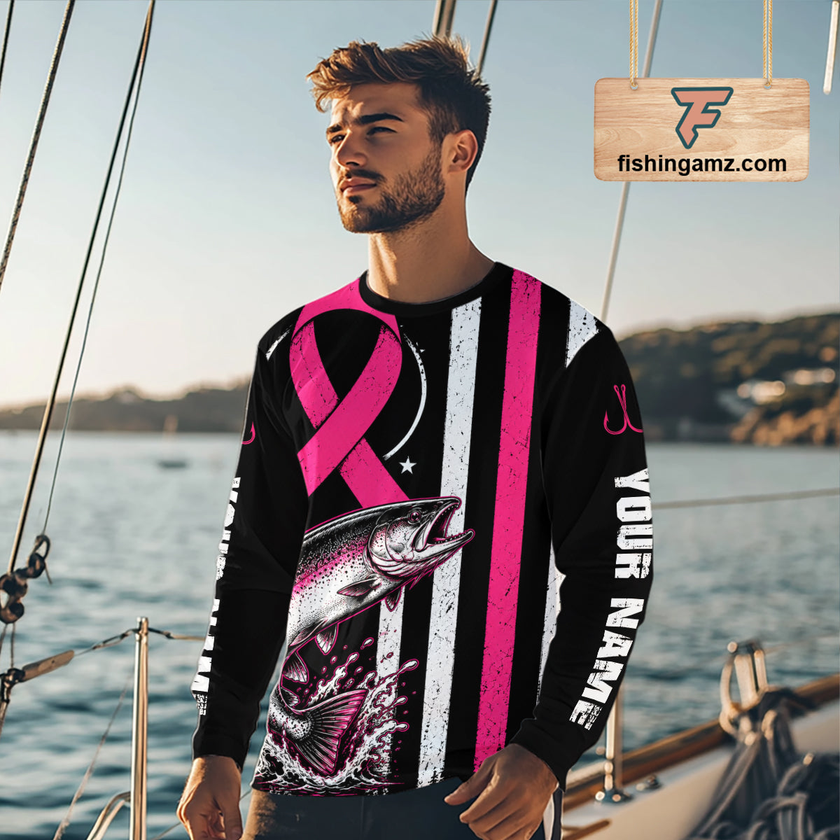 A man wearing a long-sleeve custom graphic shirt on a boat, featuring a black and white distressed American flag design with a pink ribbon, a salmon fish graphic, and 'YOUR NAME' printed on the sleeve.